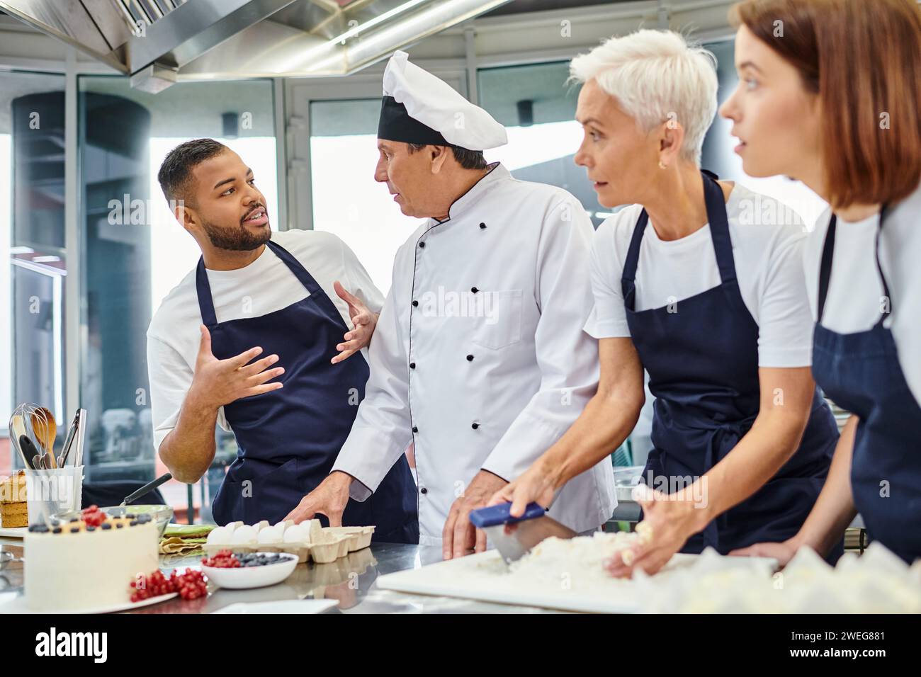 joyous african american chef in apron talking to his colleagues while they working with dough Stock Photo