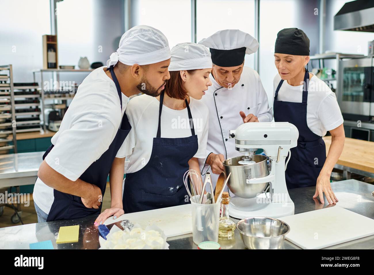 multicultural chefs in blue aprons and toques watching their chief cook