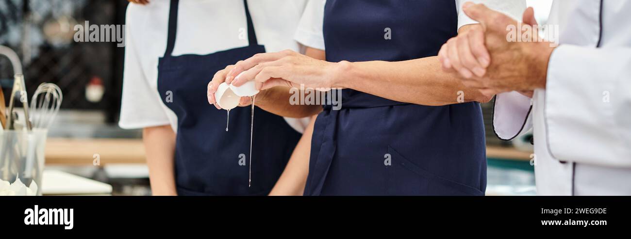 cropped view of mature woman breaking egg next to her young colleague and chief cook, banner Stock Photo