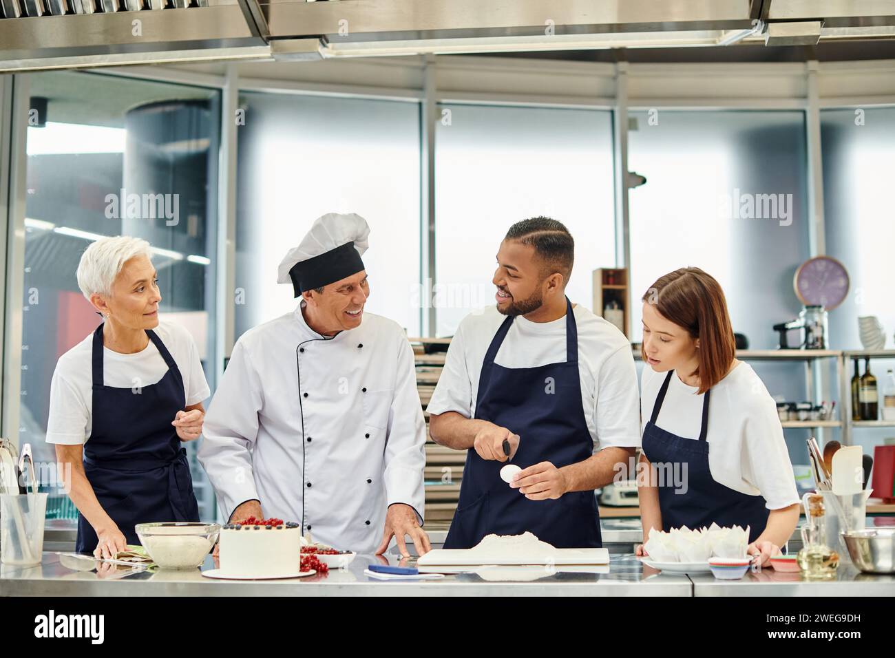 jolly handsome african american chef breaking egg and at his joyful chief cook and colleagues Stock Photo