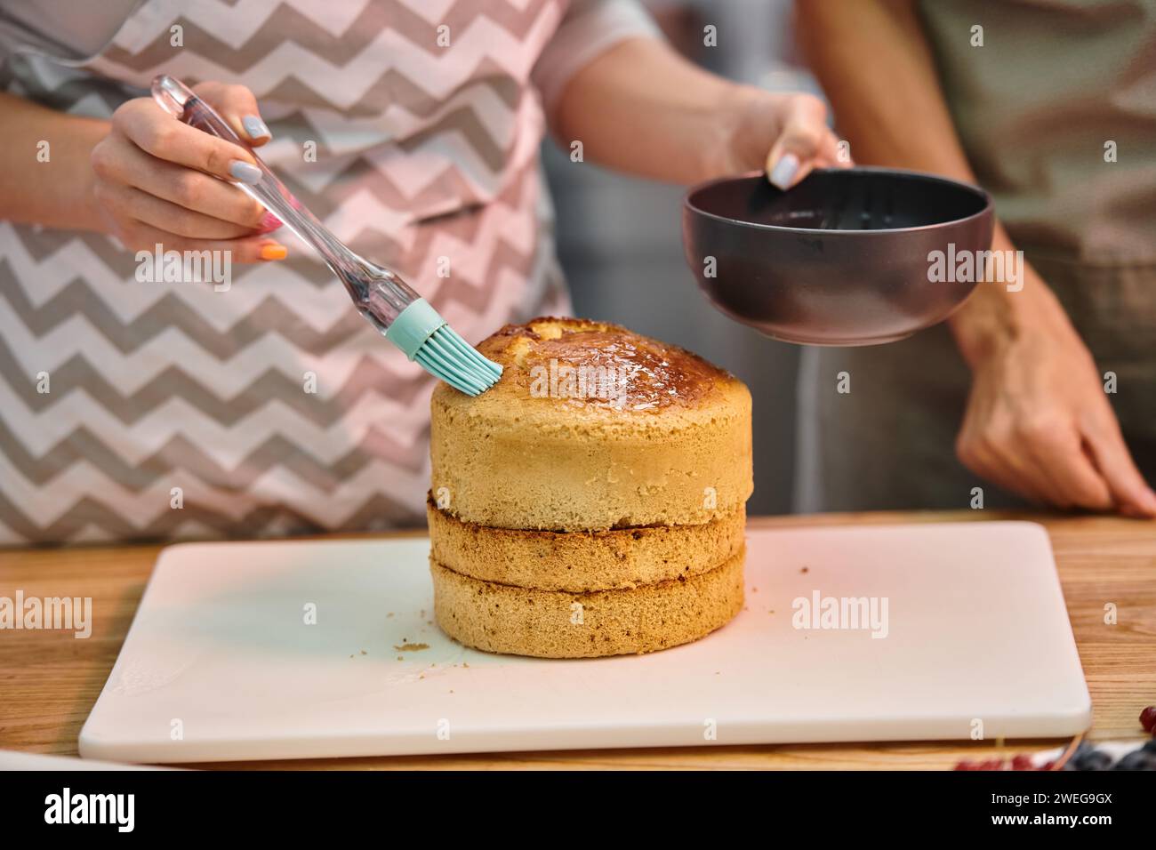 young woman with apron brushing cake with syrup on delicious cake