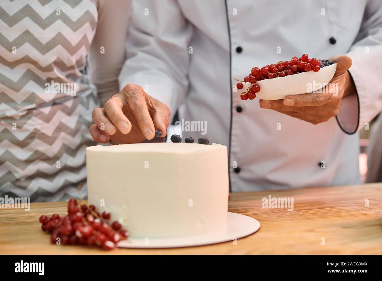 Chef Cook Cake cropped view of mature chef decorating cake with berries next to his ...