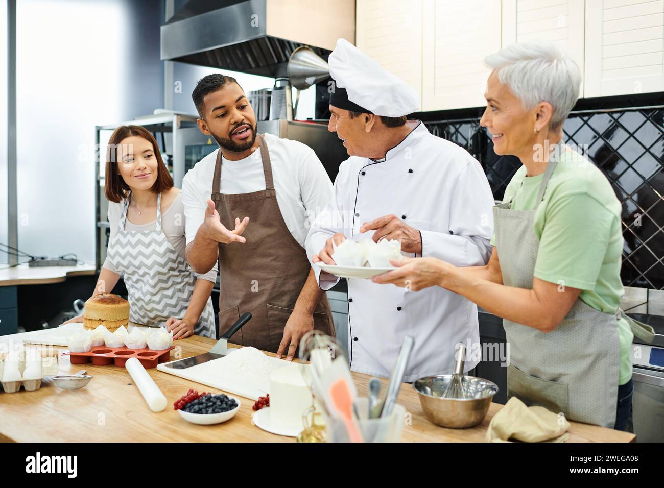 cheerful multiracial people in aprons talking to mature chef in white hat, cooking courses Stock Photo