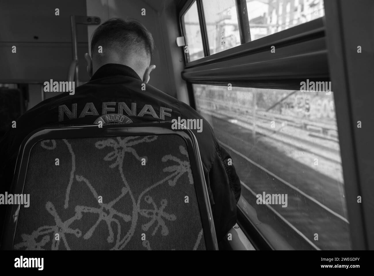 Paris, France - February 21, 2023: Young man wearing Naf Naf bomber jacket travels from suburb to city by train line RER A. Black  white photo Stock Photo