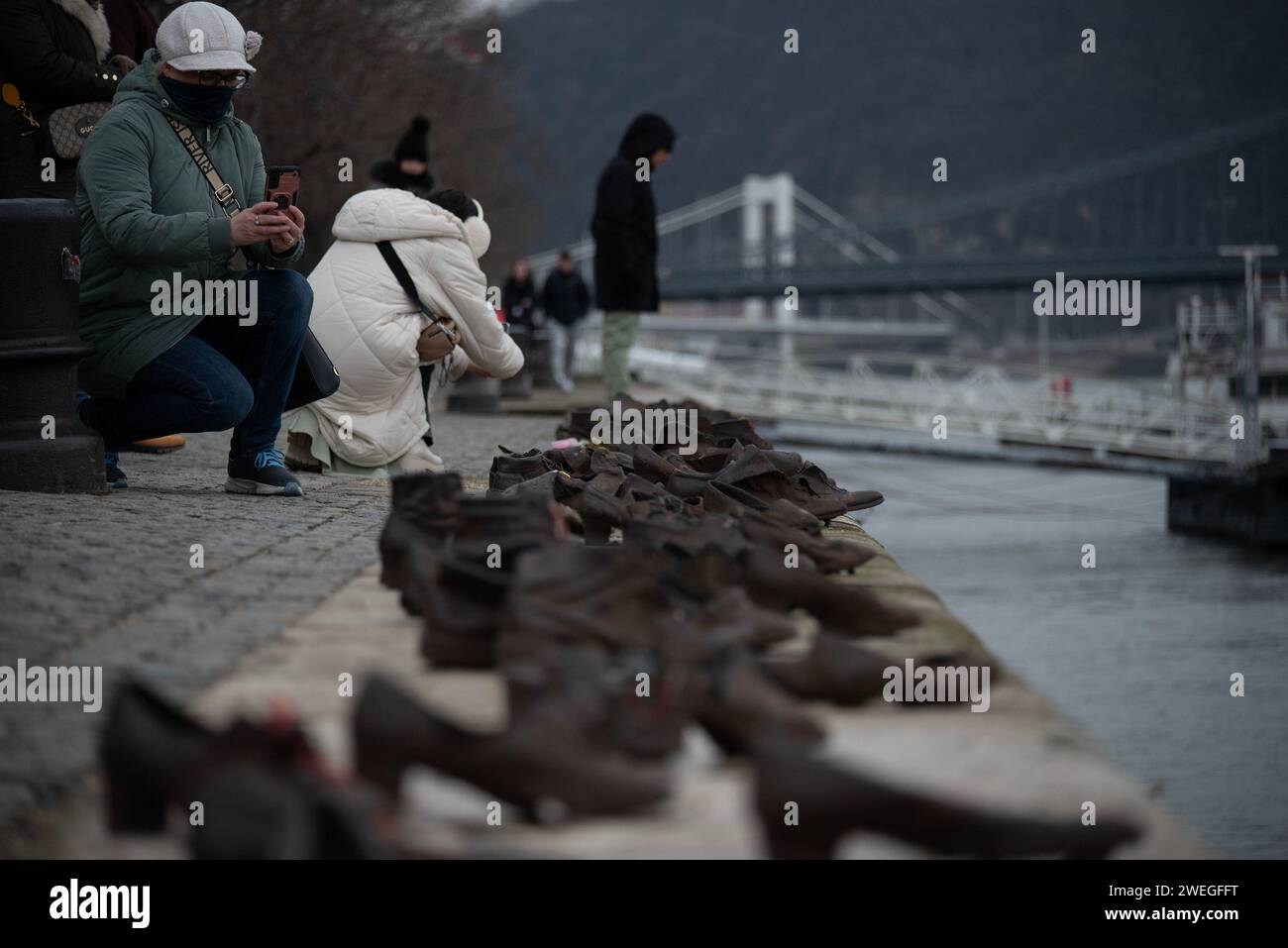 Budapest, Hungary. 24th Jan, 2024. Tourists are taking photos of the sculpture shoes on the bank of Danube River. A Sculpture of Shoes on the bank of river Danube was formed in 2005 on the East bank of the river by the Gyula Pauer. To honor the Jewish people who were shot into the river by the fascist Hungarian militia called Arrow Cross Party in 1944-45. It became a main attraction for the tourists and the people who want to show respect to the victims. (Photo by Krisztian Elek/SOPA Images/Sipa USA) Credit: Sipa USA/Alamy Live News Stock Photo