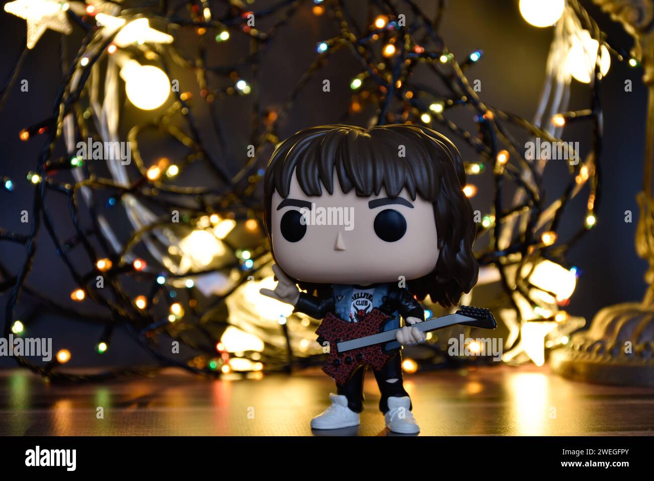 Funko Pop action figure of Eddie Munson from TV series Stranger Things. Warm and colorful garland lights, orange lighting, black background. Stock Photo