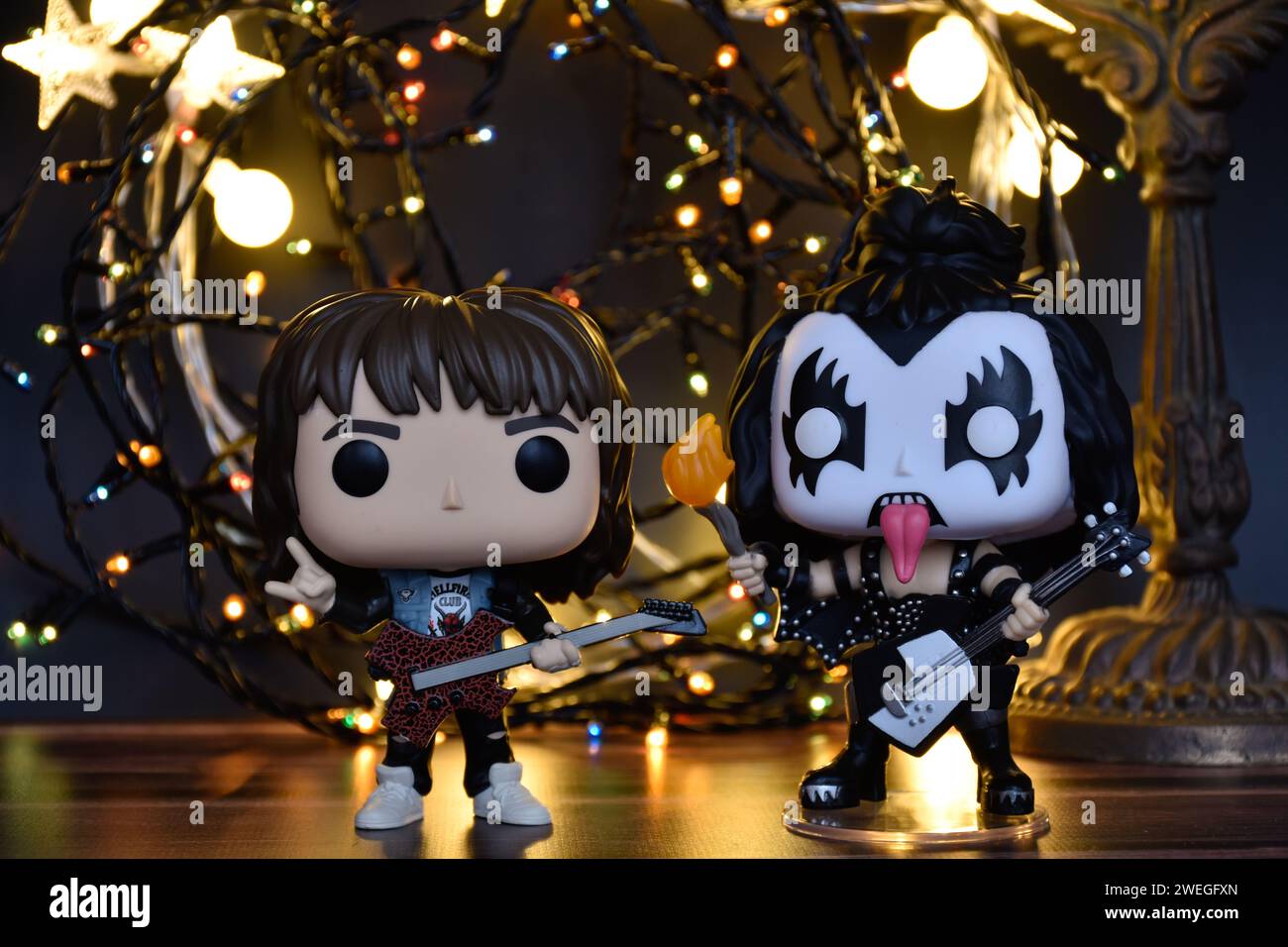 Funko Pop action figures of Eddie from TV series Stranger Things and Gene Simmons The Demon, rock band Kiss. Warm lighting, black background. Stock Photo