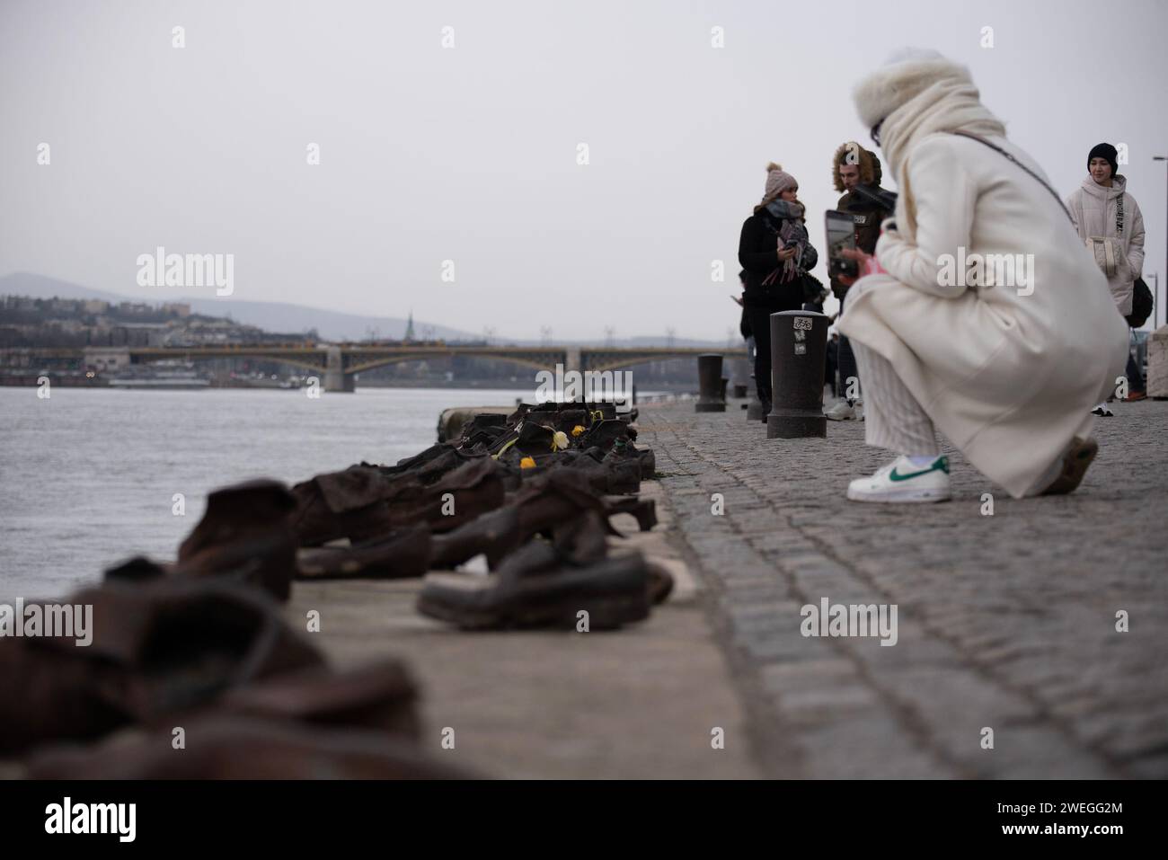 Budapest, Hungary. 24th Jan, 2024. A woman dressed in white takes photos of the shoes on the bank of Danube River. A Sculpture of Shoes on the bank of river Danube was formed in 2005 on the East bank of the river by the Gyula Pauer. To honor the Jewish people who were shot into the river by the fascist Hungarian militia called Arrow Cross Party in 1944-45. It became a main attraction for the tourists and the people who want to show respect to the victims. (Credit Image: © Krisztian Elek/SOPA Images via ZUMA Press Wire) EDITORIAL USAGE ONLY! Not for Commercial USAGE! Stock Photo