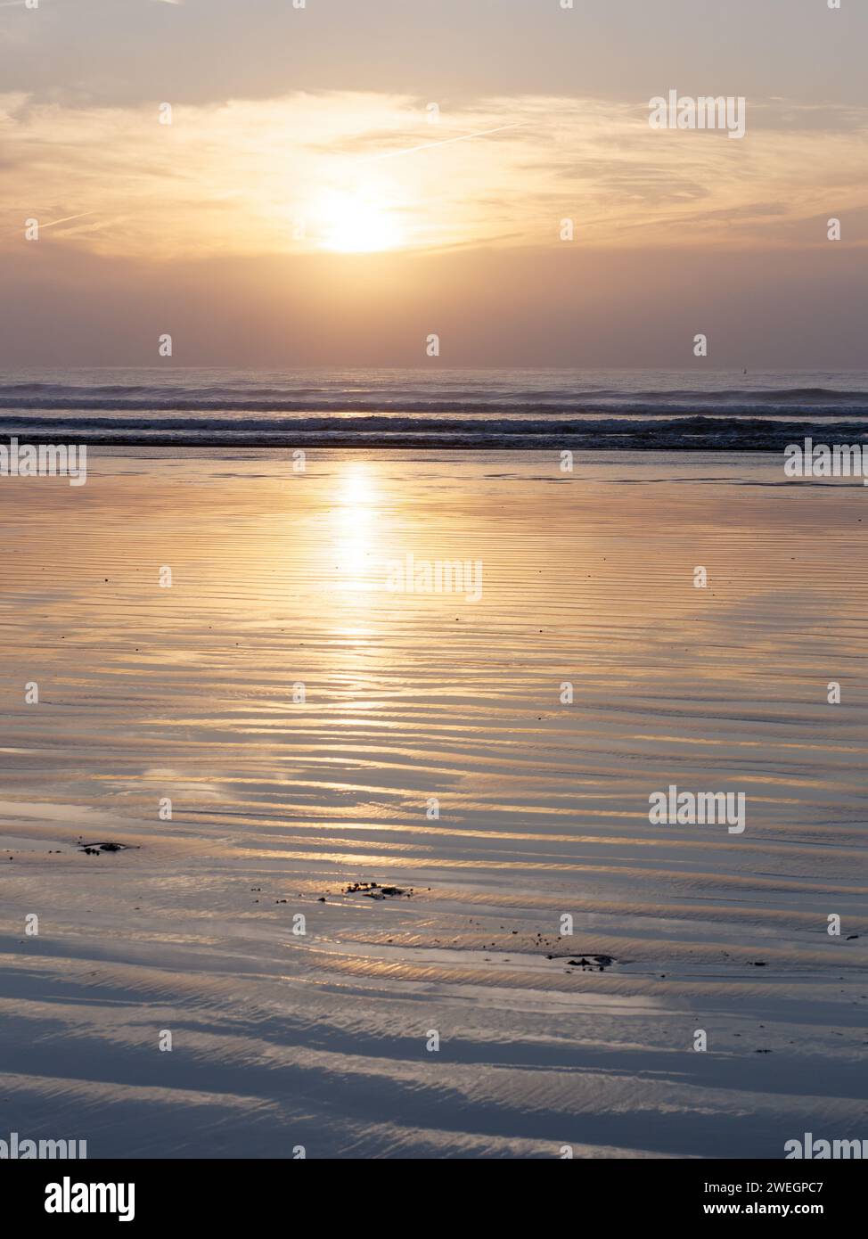 Sunset behind the clouds  reflecting in the ripples of the wet sand on a beach in Essaouira, Morocco, Jan 25th 2024 Stock Photo