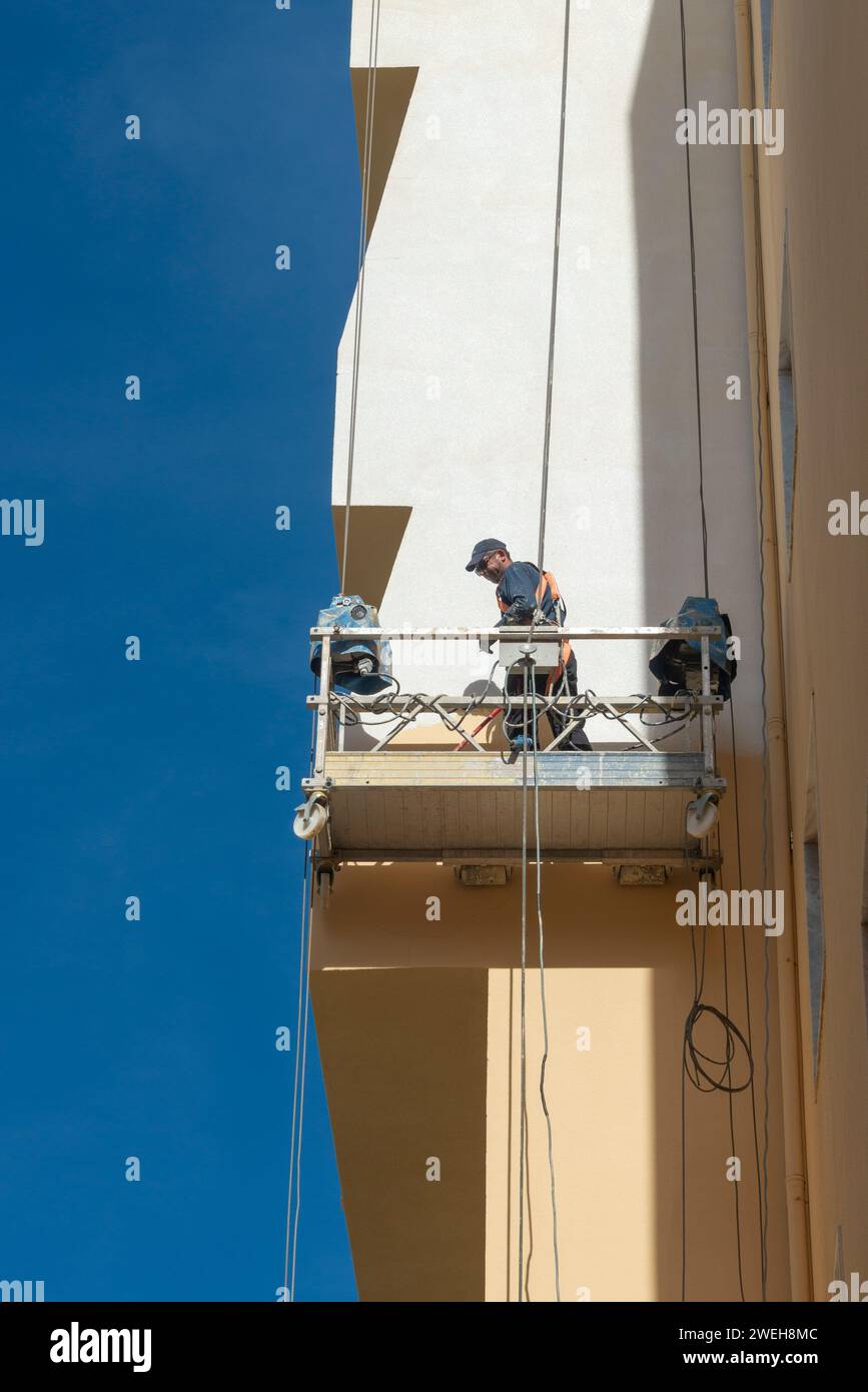 man painting the side of a tall building from a platform Stock Photo