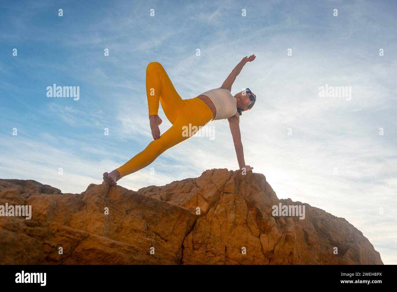 fit woman doing a side plank yoga pose on a rock, blue sky background Stock Photo