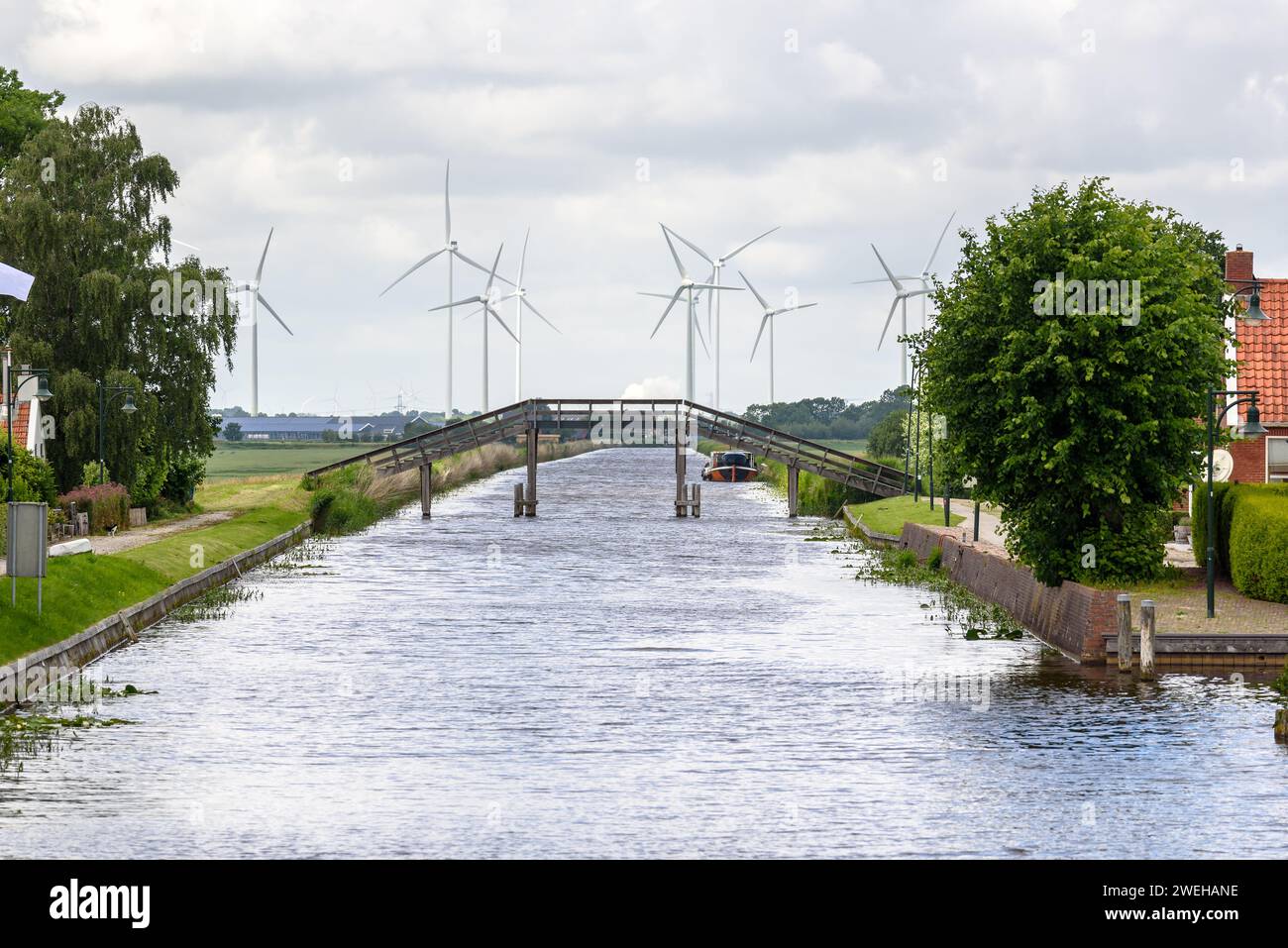 Wooden footbridge over a canal with wind turbines in background on a cloudy summer day Stock Photo