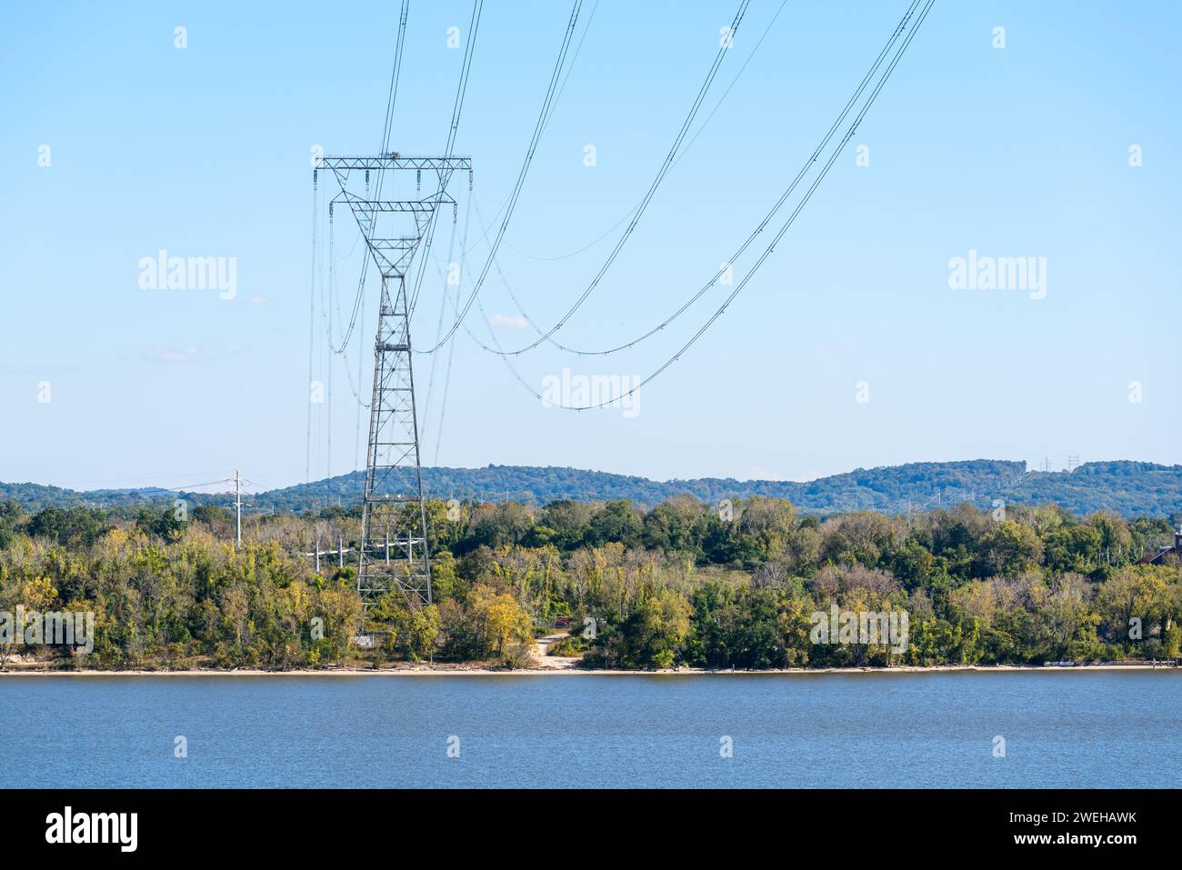 Tall electricity pylon supporting high voltage lines on the bank of a river on a sunny autumn day Stock Photo