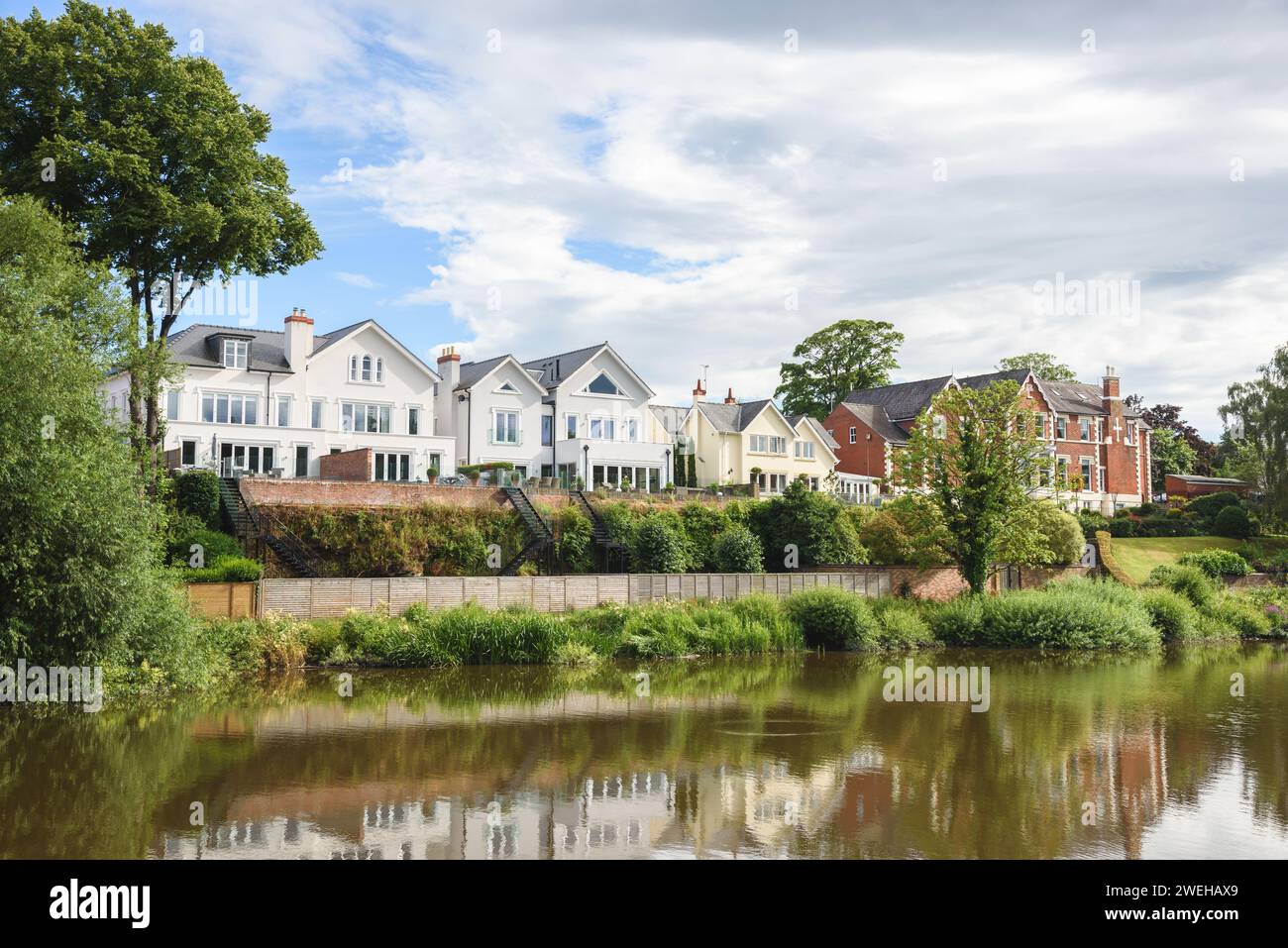 Row of modern houses on the bank of a river on a partly cloudy summer ...