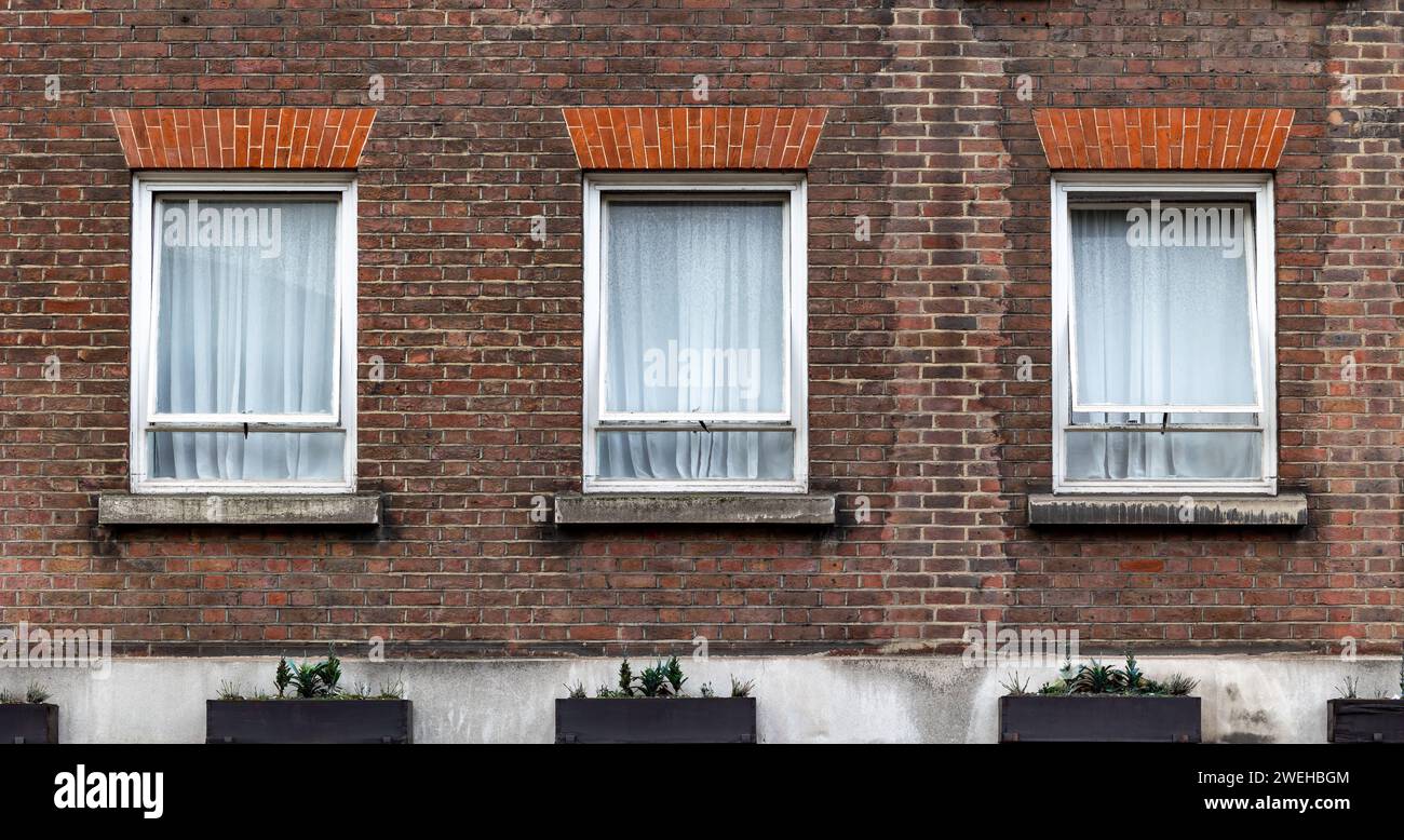three aligned classic white windows of typical london architecture with red brick wall Stock Photo