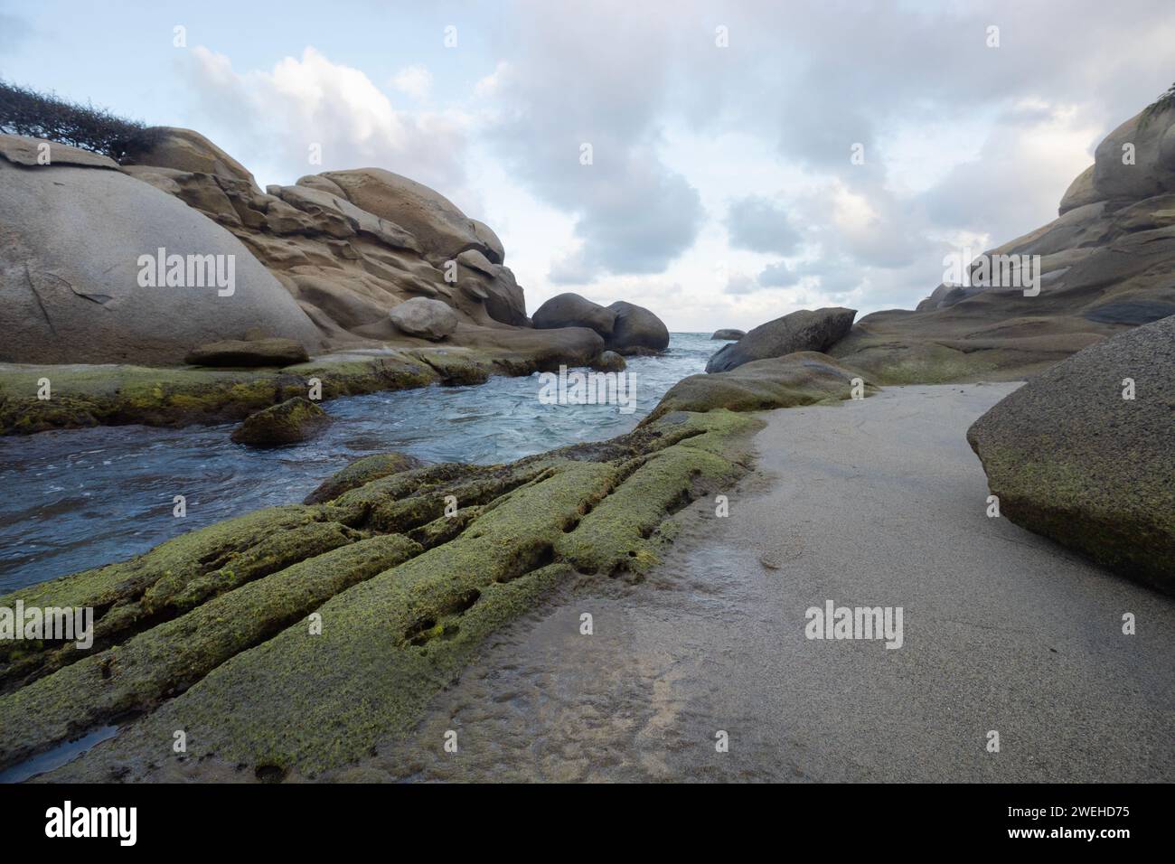 Beautiful green mossy rocks peaks into caribbean sea with cloudy sky Stock Photo