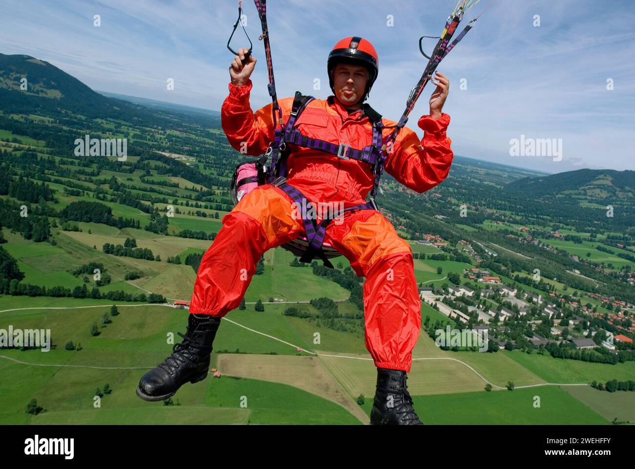 a man in signal red overalls hangs from a paraglider high above the meadows near Lenggries, pilot's perspective, Bavaria, Germany, Europe Stock Photo
