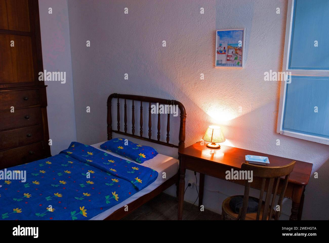 Bed and wooden table with illuminated bedside lamp in the room of a small, simple hotel or guesthouse in Santa Cruz de la Palma, La Palma, Canary Stock Photo