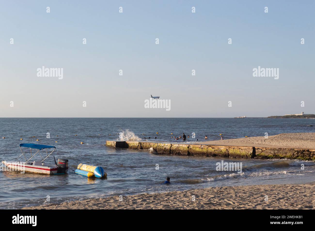 An airplane landing on simon bolivar international airport viewed from a resort beach with banana boat ride a shore in sunset golden hour Stock Photo