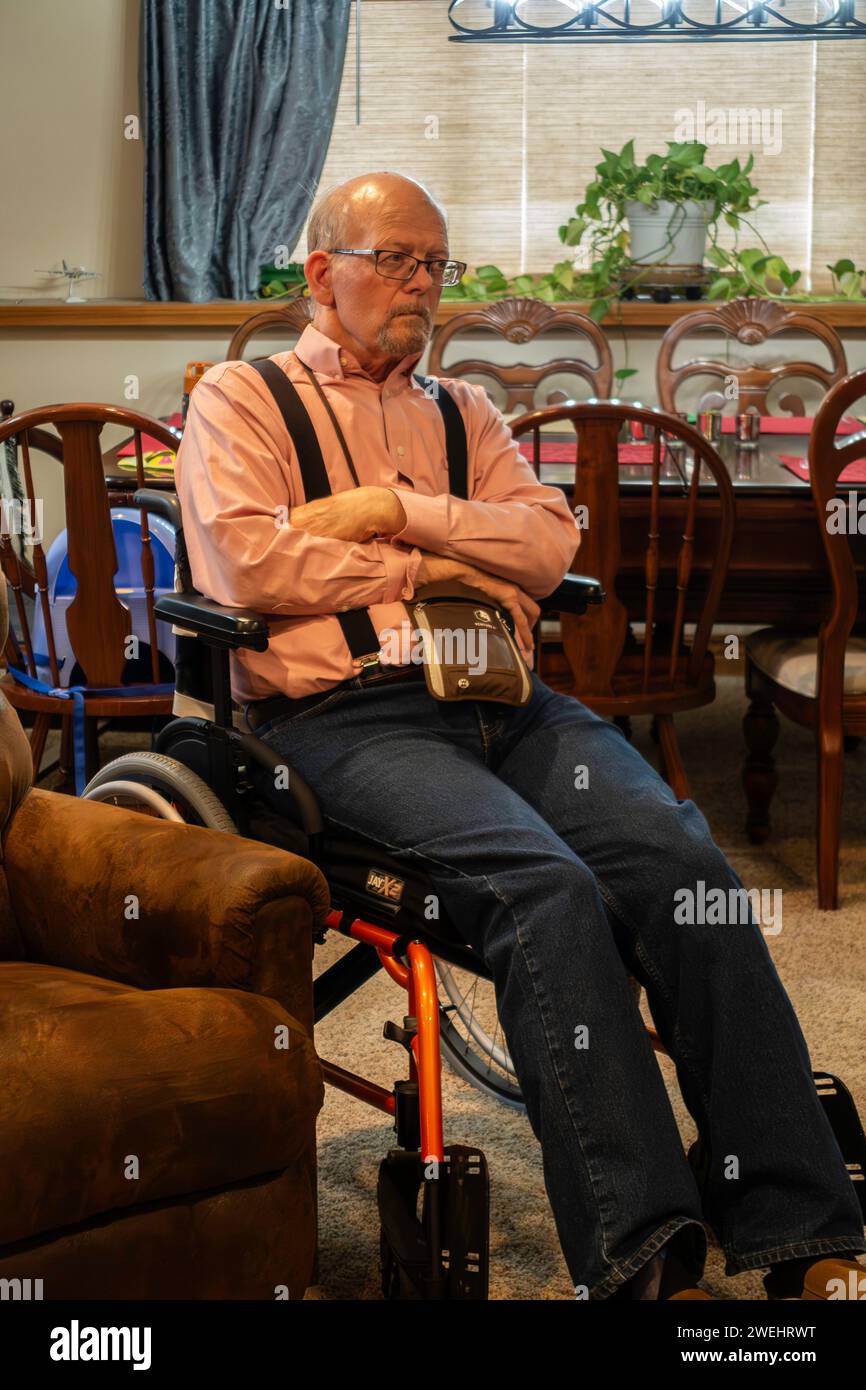 67 year old balding Caucasian handicapped senior adult man wearing glasses, sitting in a wheelchair & looking away. USA. Stock Photo