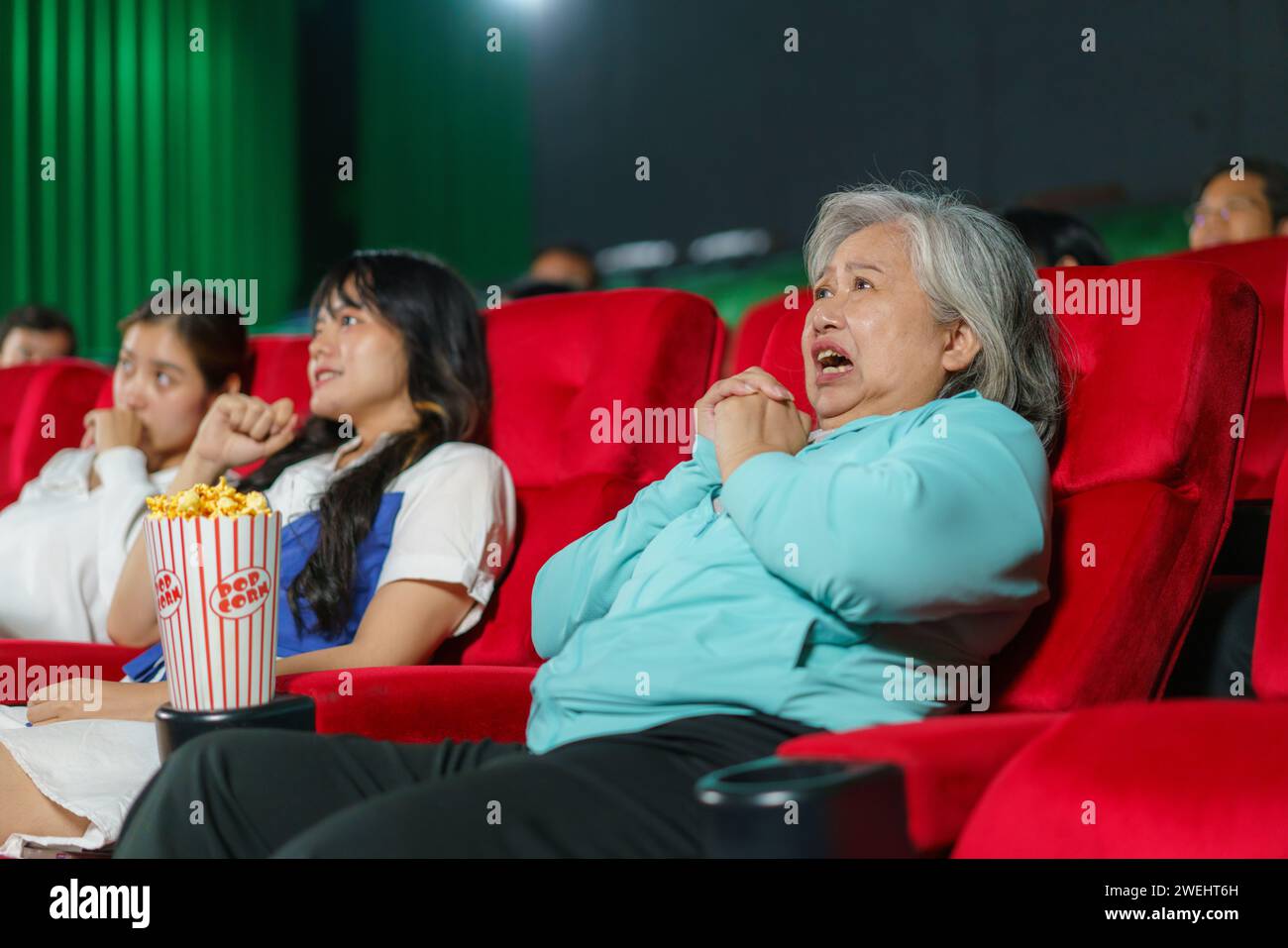 elderly Asian woman as she expresses genuine astonishment while watching a horror film in the cinema Stock Photo