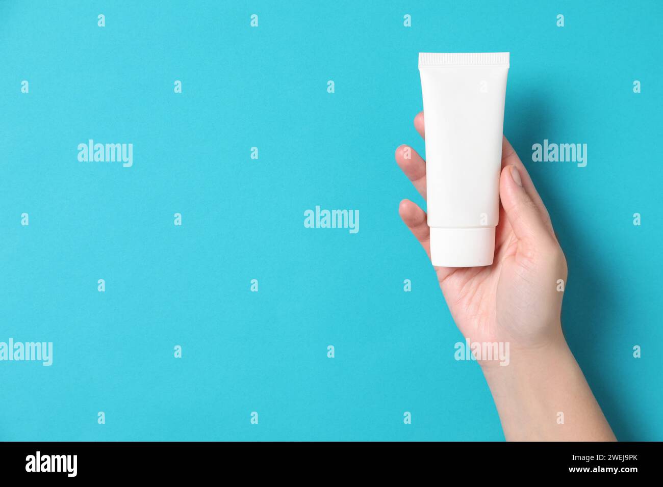 Woman with tube of hand cream on light blue background, top view. Space