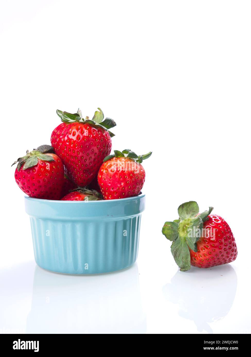 Strawberries piled in a blue bowl against a white background with a ...