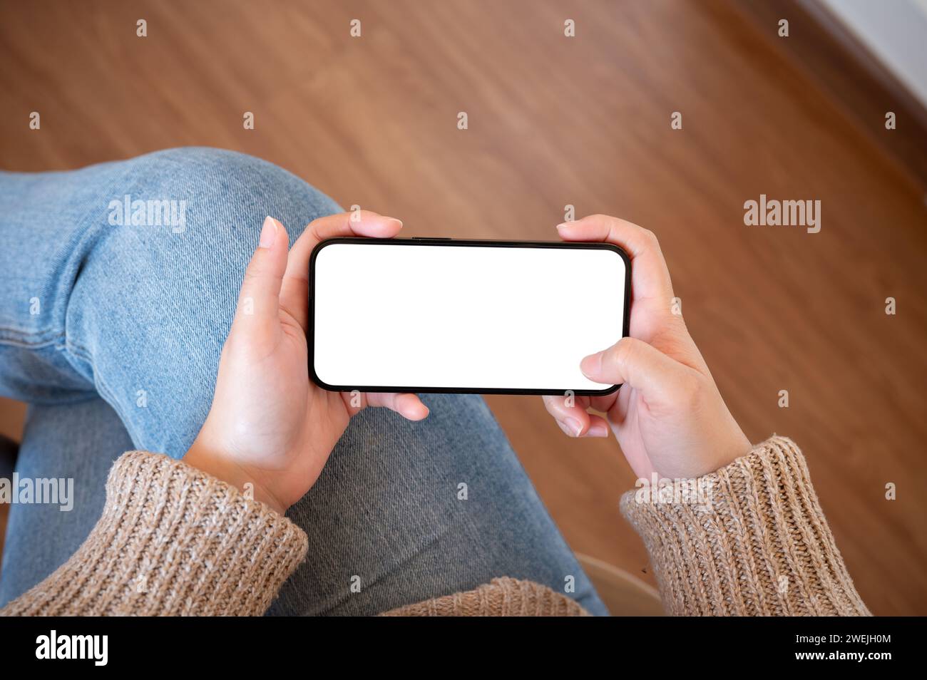 Close-up image of a woman holding a white-screen smartphone mockup in a horizontal position indoors. watching videos, playing a mobile game Stock Photo