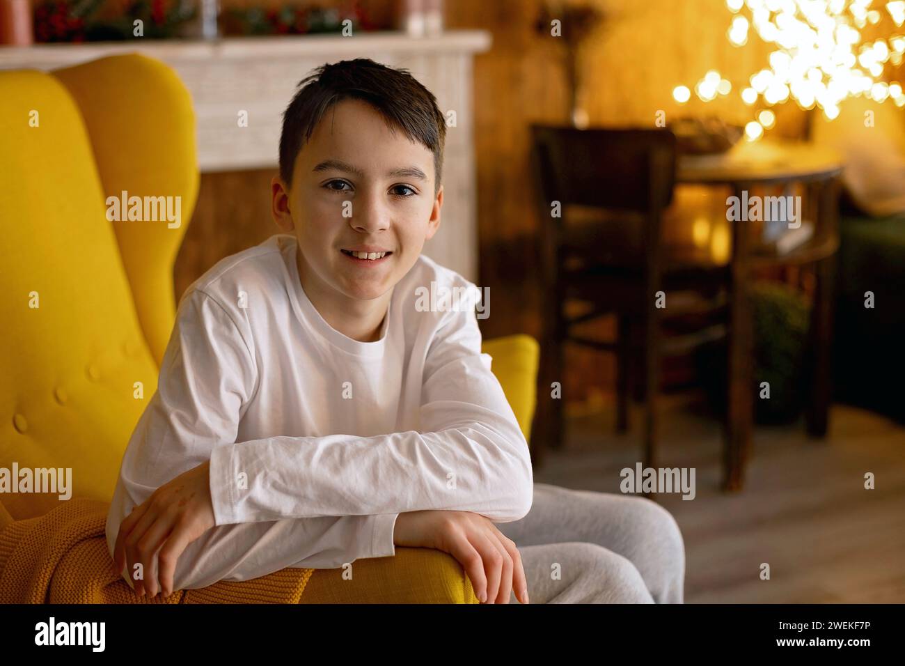Teenage child, boy, sitting in cozy armchair at home, smiling at camera Stock Photo