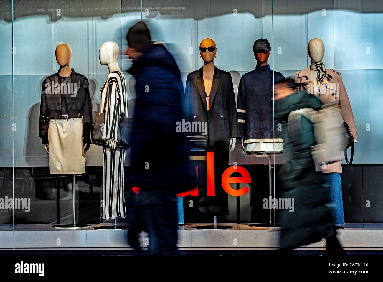 A group of individuals strolling by a shop adorned with a captivating display of mannequins. Stock Photo
