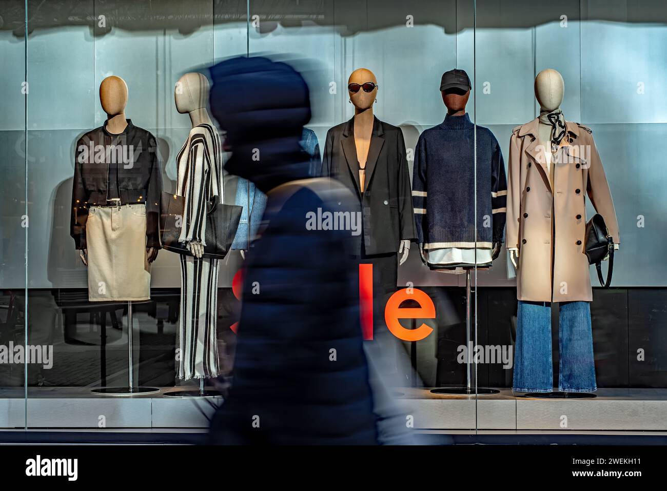 A group of individuals strolling by a shop adorned with a captivating display of mannequins. Stock Photo
