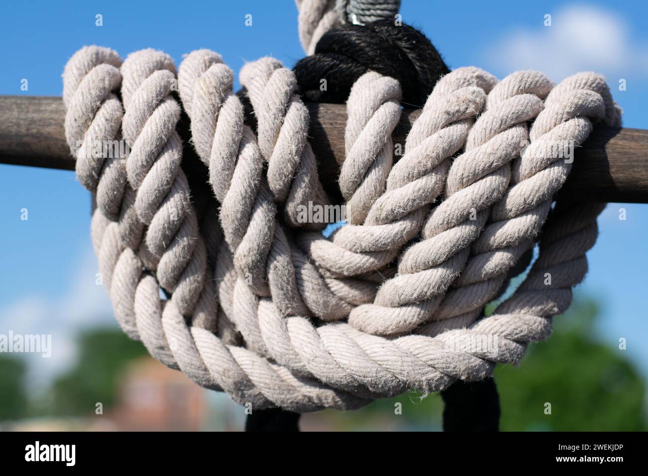 A thick, white rope is expertly coiled around a sturdy mooring post, contrasting against the vibrant blue sky of a calm day. Stock Photo