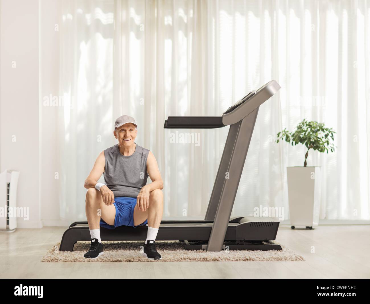 Elderly man sitting on a treadmill at home Stock Photo
