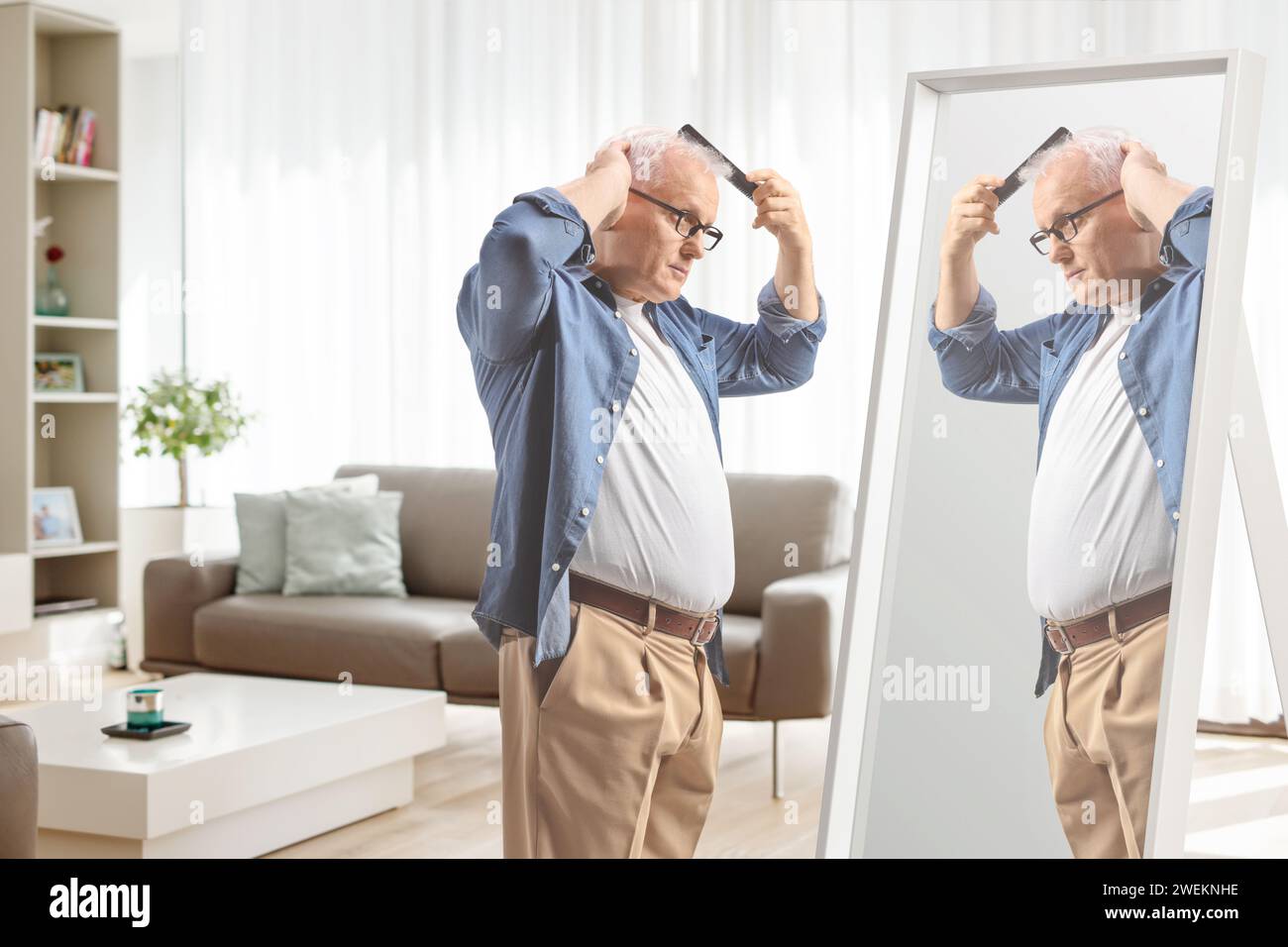 Mature man combing hair in front of a mirror at home, hair loss concept Stock Photo
