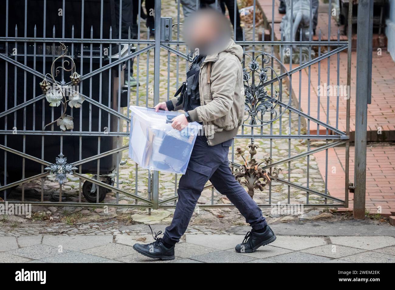 Berlin, Germany. 26th Jan, 2024. A police officer carries a box in front of a villa belonging to a clan in the Berlin district of Buckow in the Neukölln borough. Due to the attack on a policewoman by a clan member on New Year's Eve, there was another police operation at the villa of the extended family. According to the police, there is no connection with the planned eviction of the villa by the Neukölln district. Credit: Christoph Soeder/dpa - ATTENTION: Police officer has been pixelated for legal reasons/dpa/Alamy Live News Stock Photo