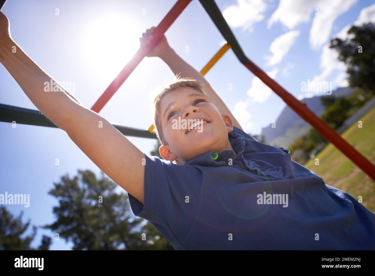 Child, monkey bars and energy on playground, smiling and obstacle course on outdoor adventure at park. Happy male person, active and exercise on Stock Photo