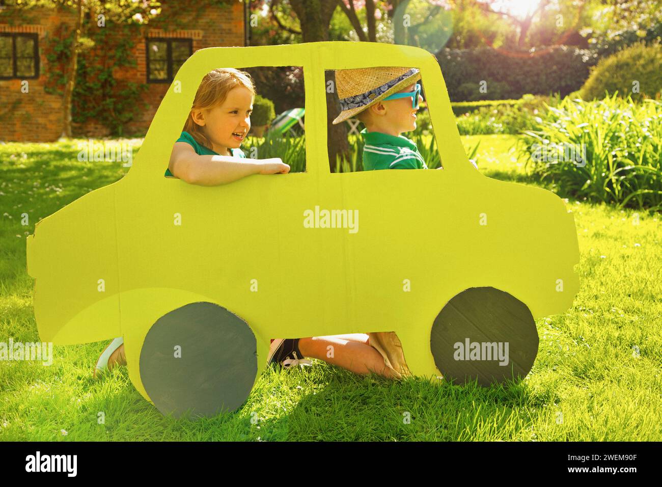 Boy and Girl Kneeling behind Cardboard Cut Out in Shape of Car Stock