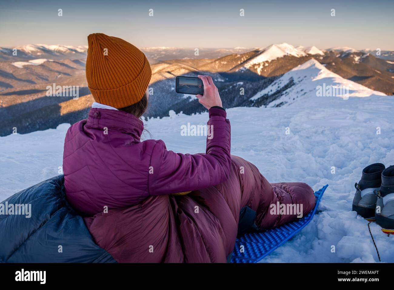 Woman in Sleeping Bag Using Mobile Phone Capturing The Snow Mountains Stock Photo