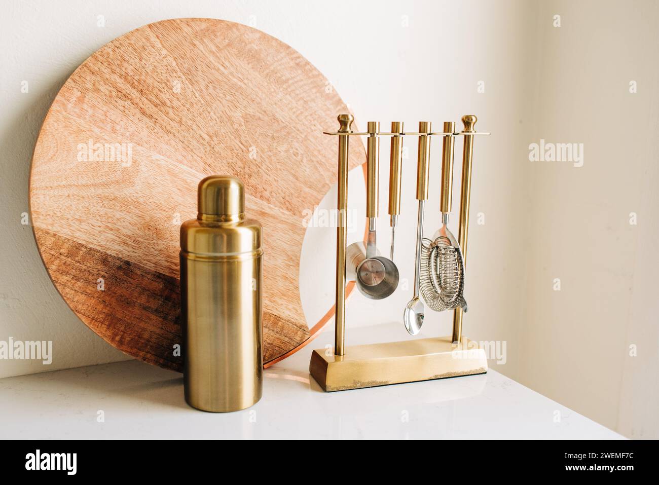 Wooden Cutting Board and Gold Cocktail Mixing Set on White Counter Stock Photo