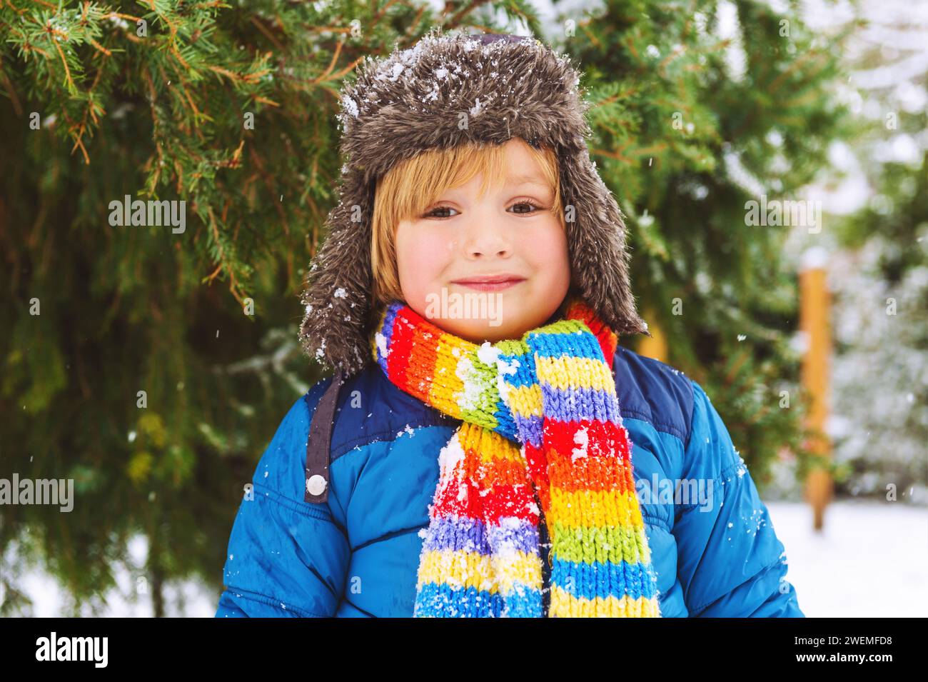 Cute little boy playing in winter park. Kid having fun outdoors, running on snow, wearing warm blue jacket, hat and scarf Stock Photo
