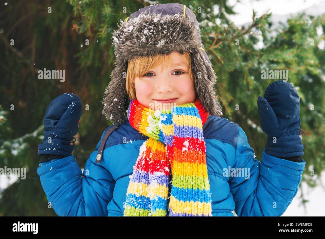 Cute little boy playing in winter park. Kid having fun outdoors, running on snow, wearing warm blue jacket, hat and scarf Stock Photo