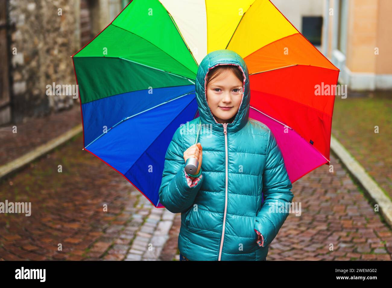 Outdoor portrait of a cute little girl, wearing warm green jacket, holding big colorful umbrella Stock Photo