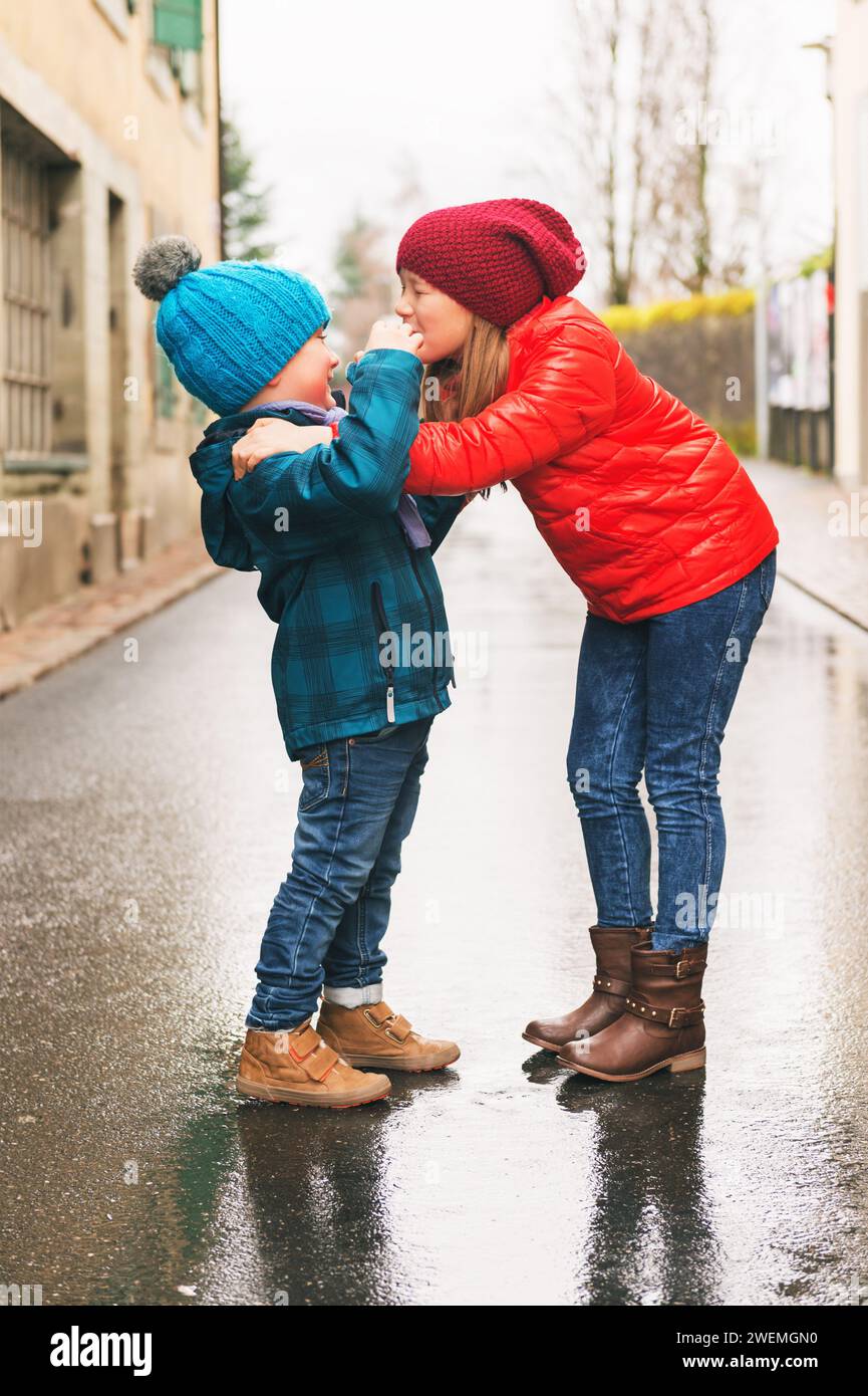 Big sister giving a hug to her small brother, kids wearing bright warm jackets Stock Photo