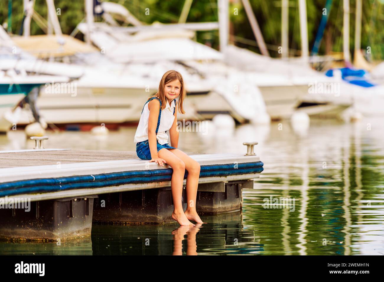 Cute little kid girl resting by the lake, sitting on pier Stock Photo ...