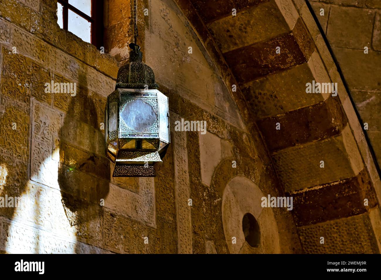 Beam of light shone through a small window in the interior of Deir Al Kamar Municipality, Lebanon. onto a bronze lantern, casting a shadow on the wall. Stock Photo
