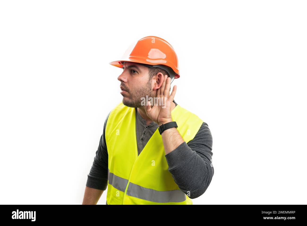 Adult model as curious male builder making listening secret eavesdropping gesture with hand to ear isolated on white studio background Stock Photo