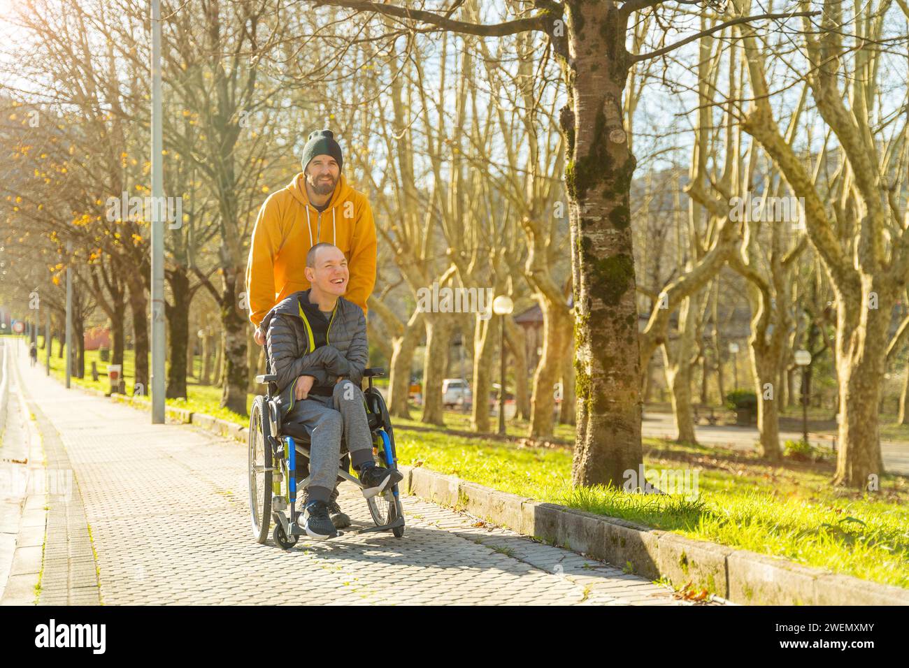 Disabled man and friend along a path in a park during a sunny day of winter Stock Photo