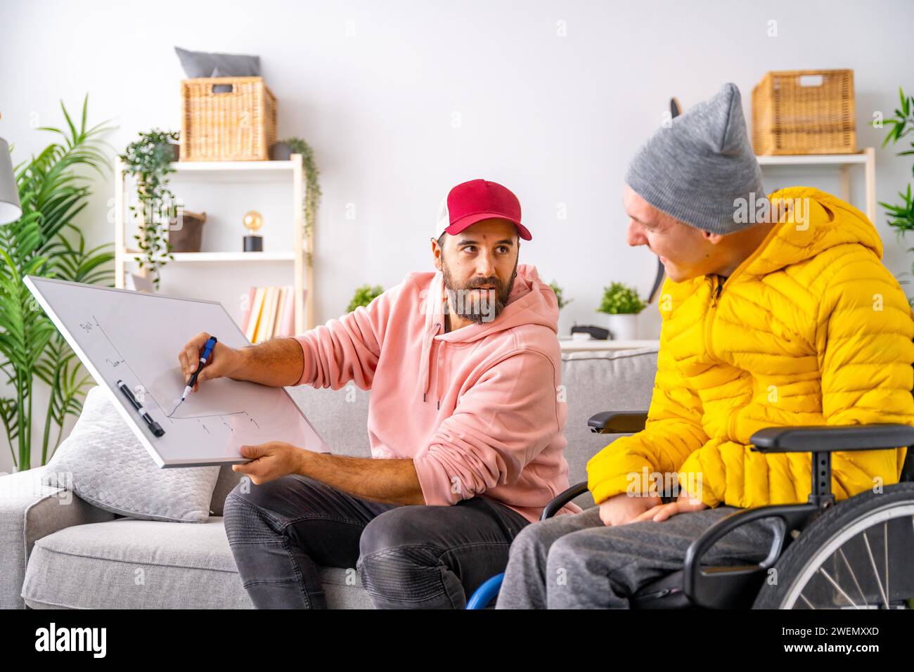 Man teaching economy to a disabled man drawing a graphic in a white board at home Stock Photo