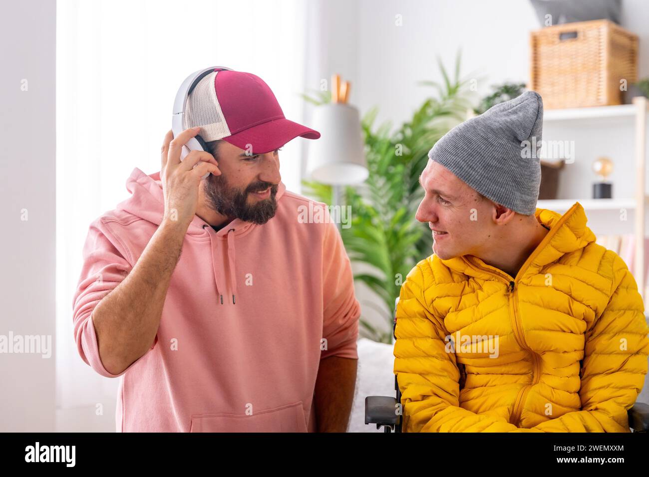 Man listening to music using headphones next to a disabled friend in wheelchair at home Stock Photo