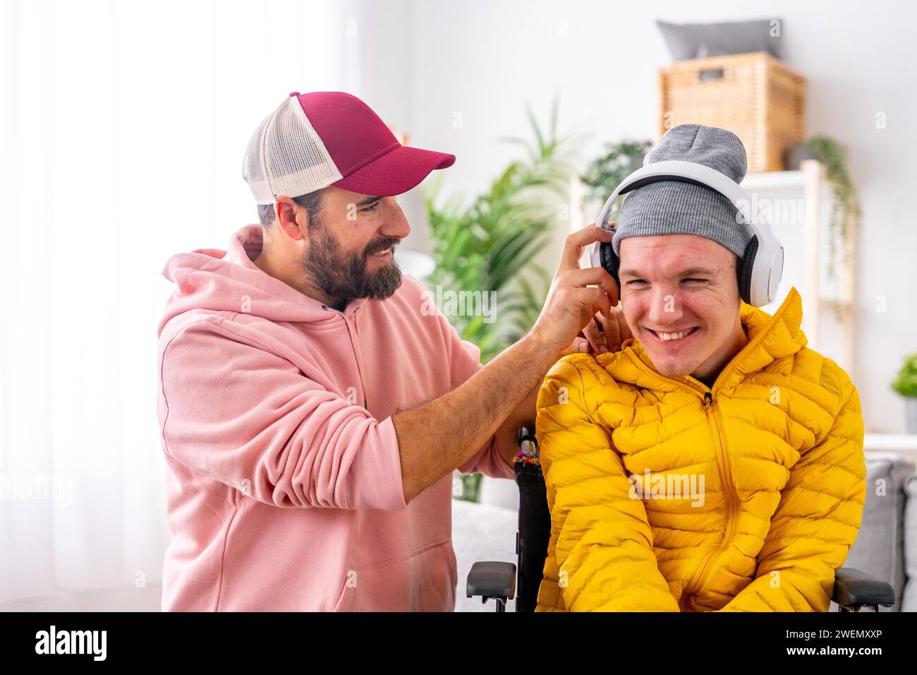 Happy disabled man listening to music using headphones with caregiver at home Stock Photo